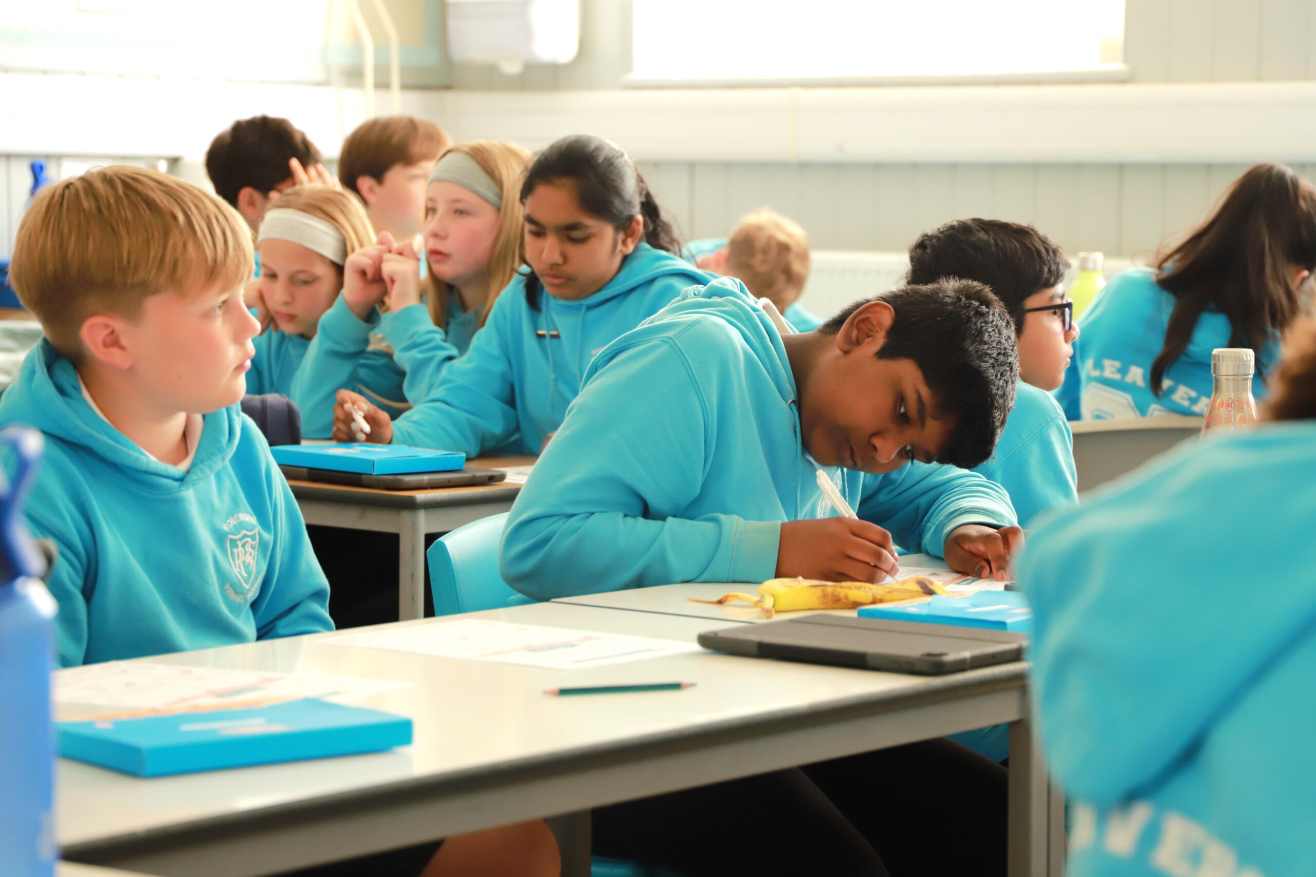 A young boy writing with some other students around him