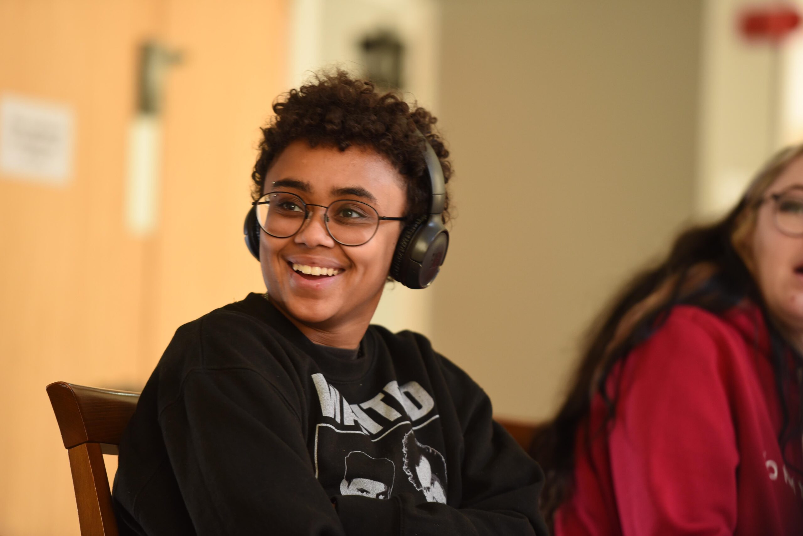 Young person wearing glasses and headphones round their neck sat smiling