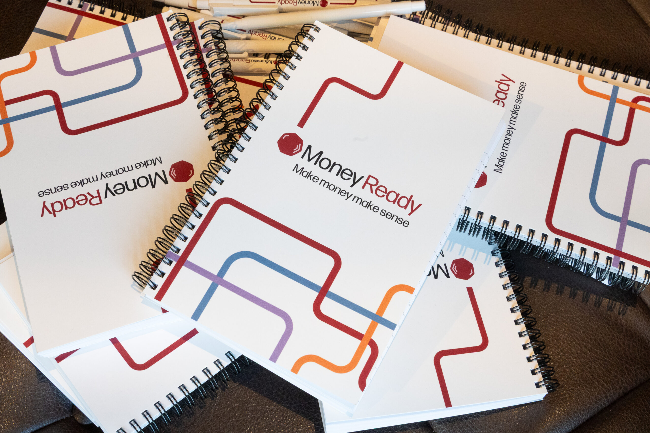 A pile of ringbound A5 notepads with the Money Ready branding on a white cover