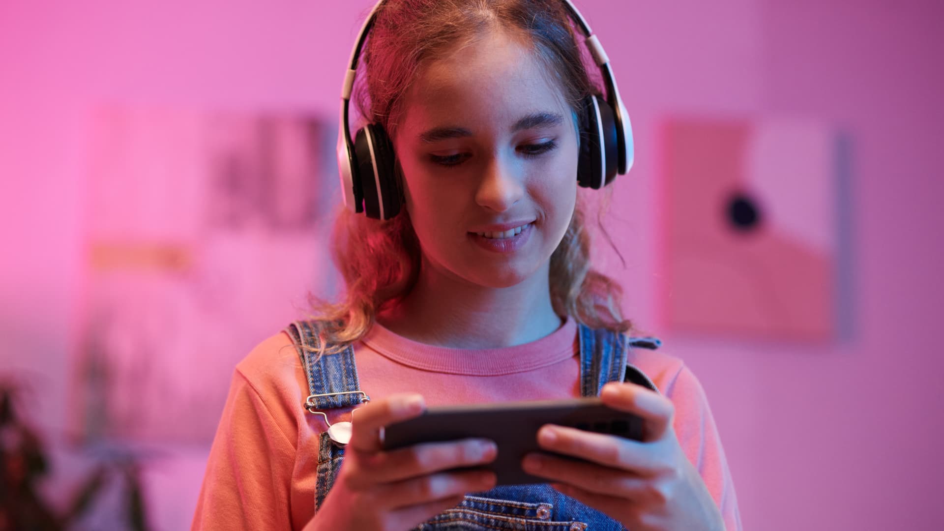 Teenage girl wearing over-the-head headphones and looking at a video on her mobile phone