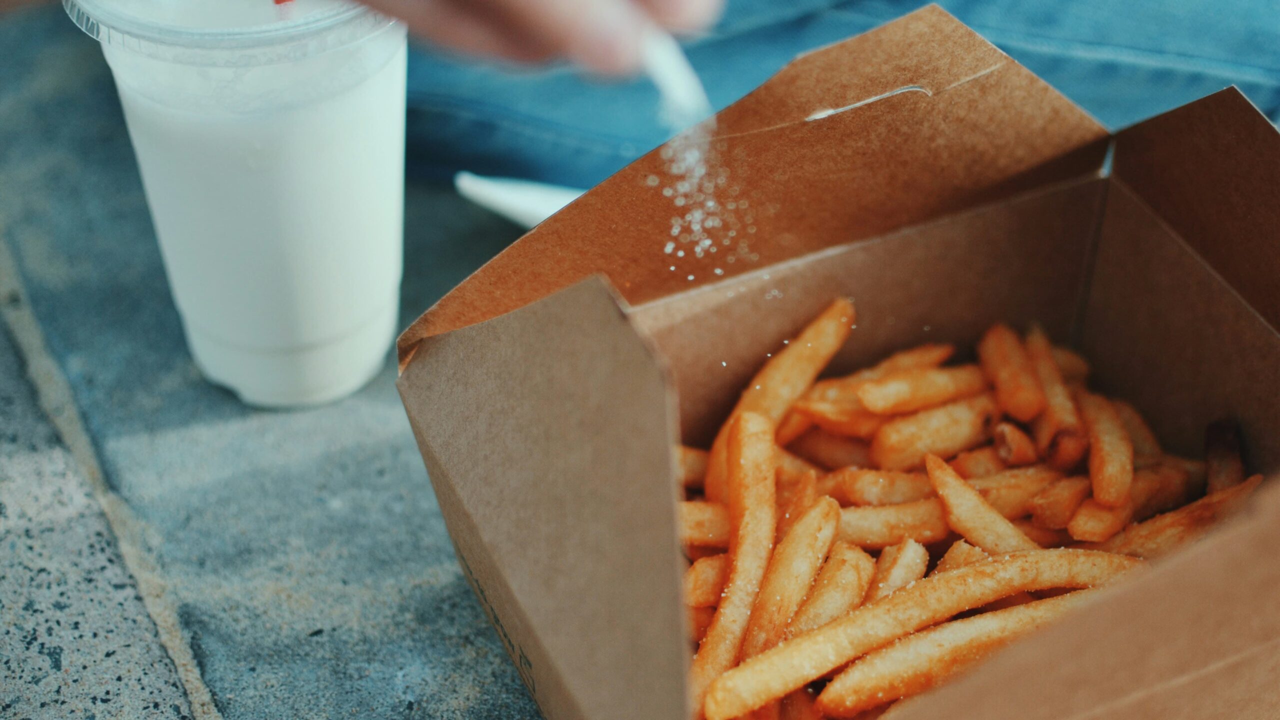 Box of french fries with someone sprinkling salt over them