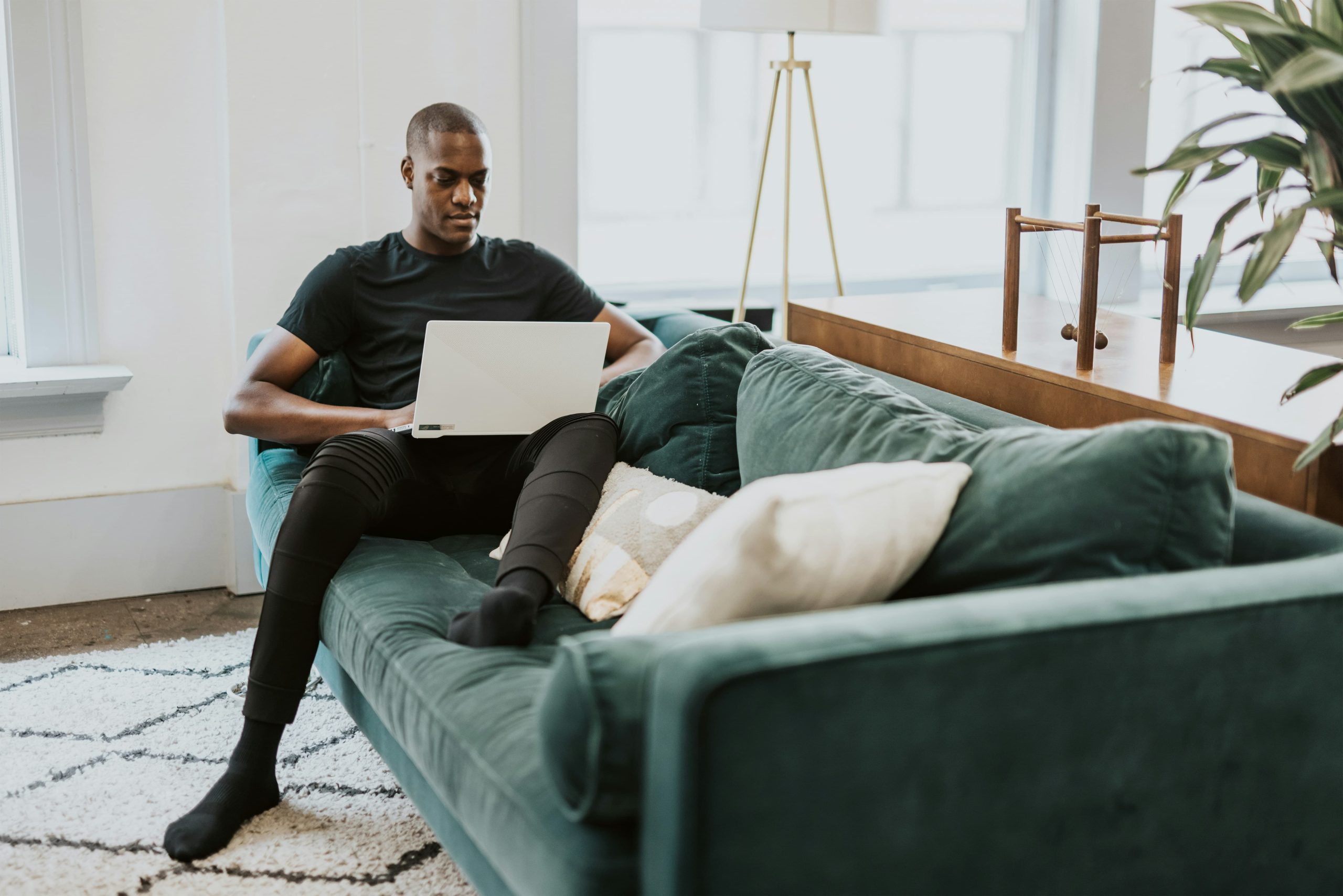 A young man sat on a green sofa working on a laptop