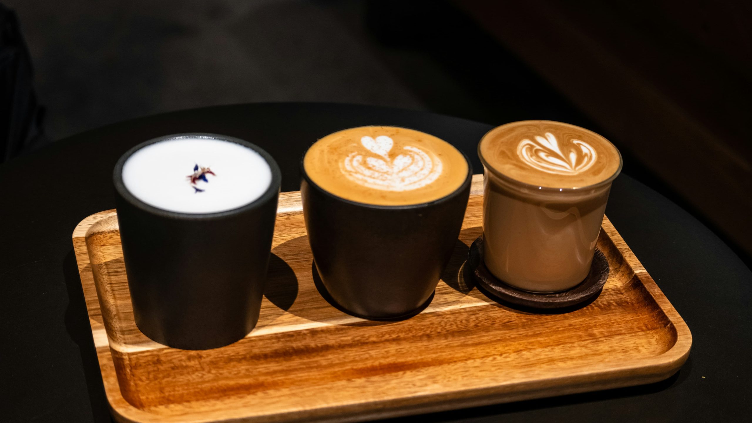 Three various coffees on a wooden board: latte, flat white, cappucino