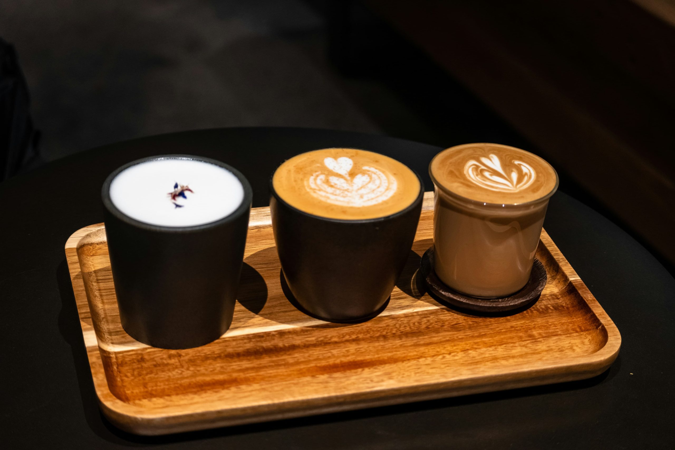 Three various coffees on a wooden board: latte, flat white, cappucino