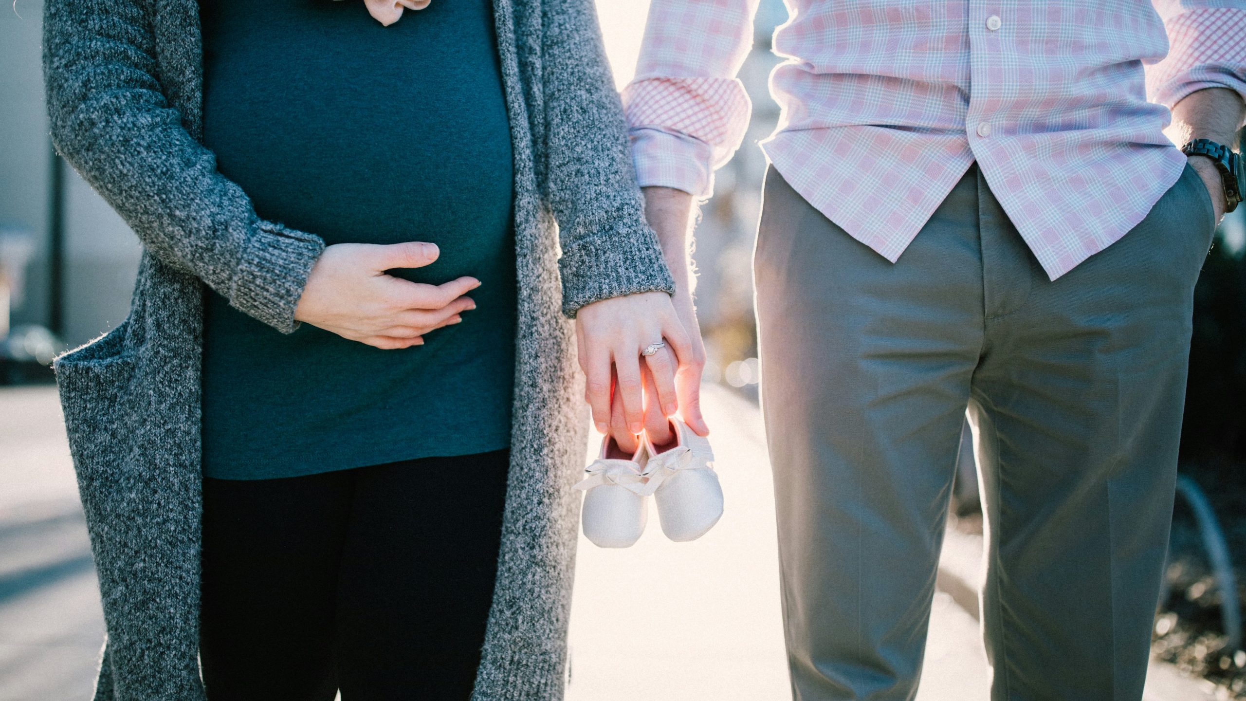 Pregnant person and partner holding hands and holding baby booties