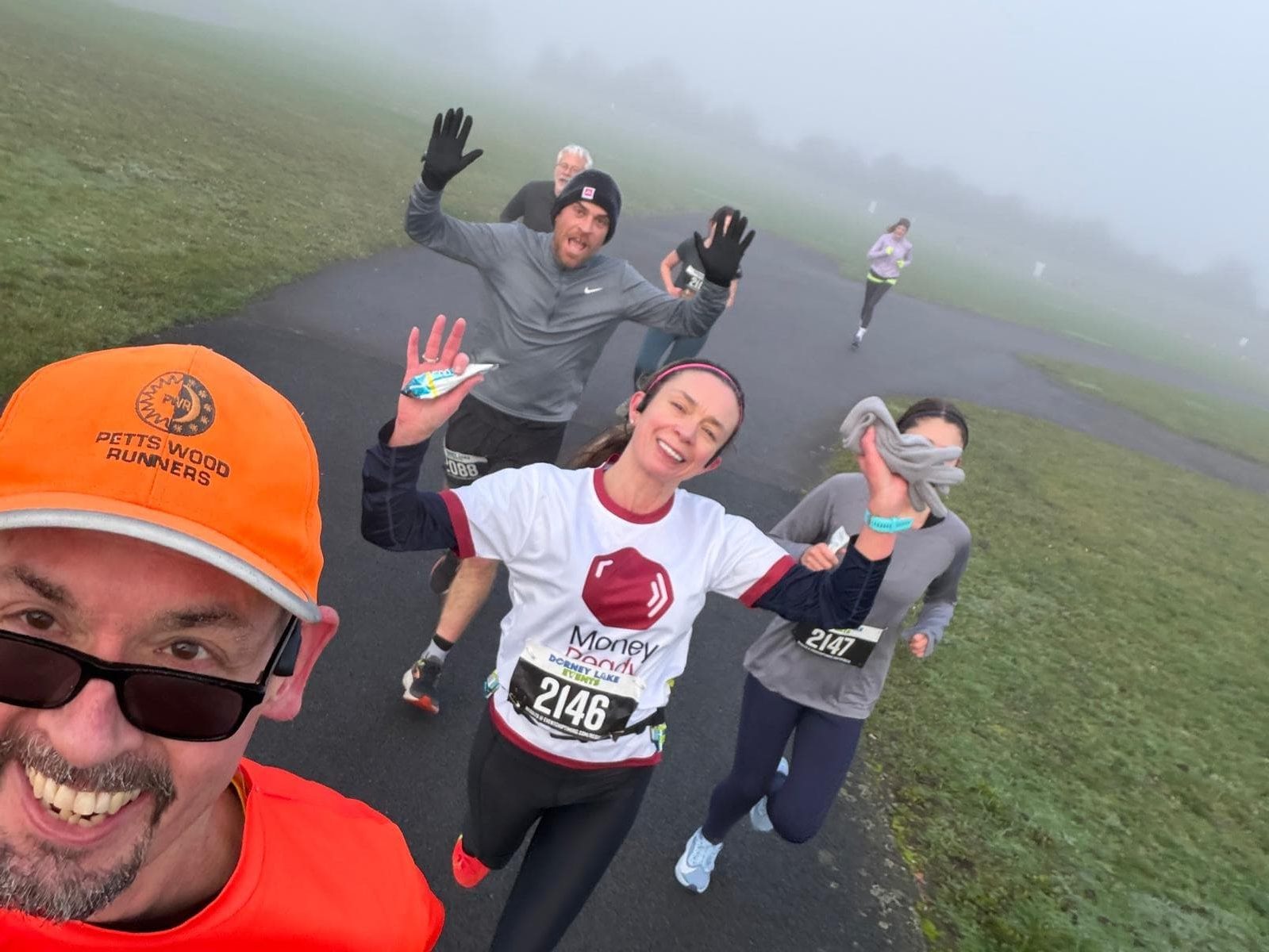 Runners on a foggy run through a park smiling and waving at the camera