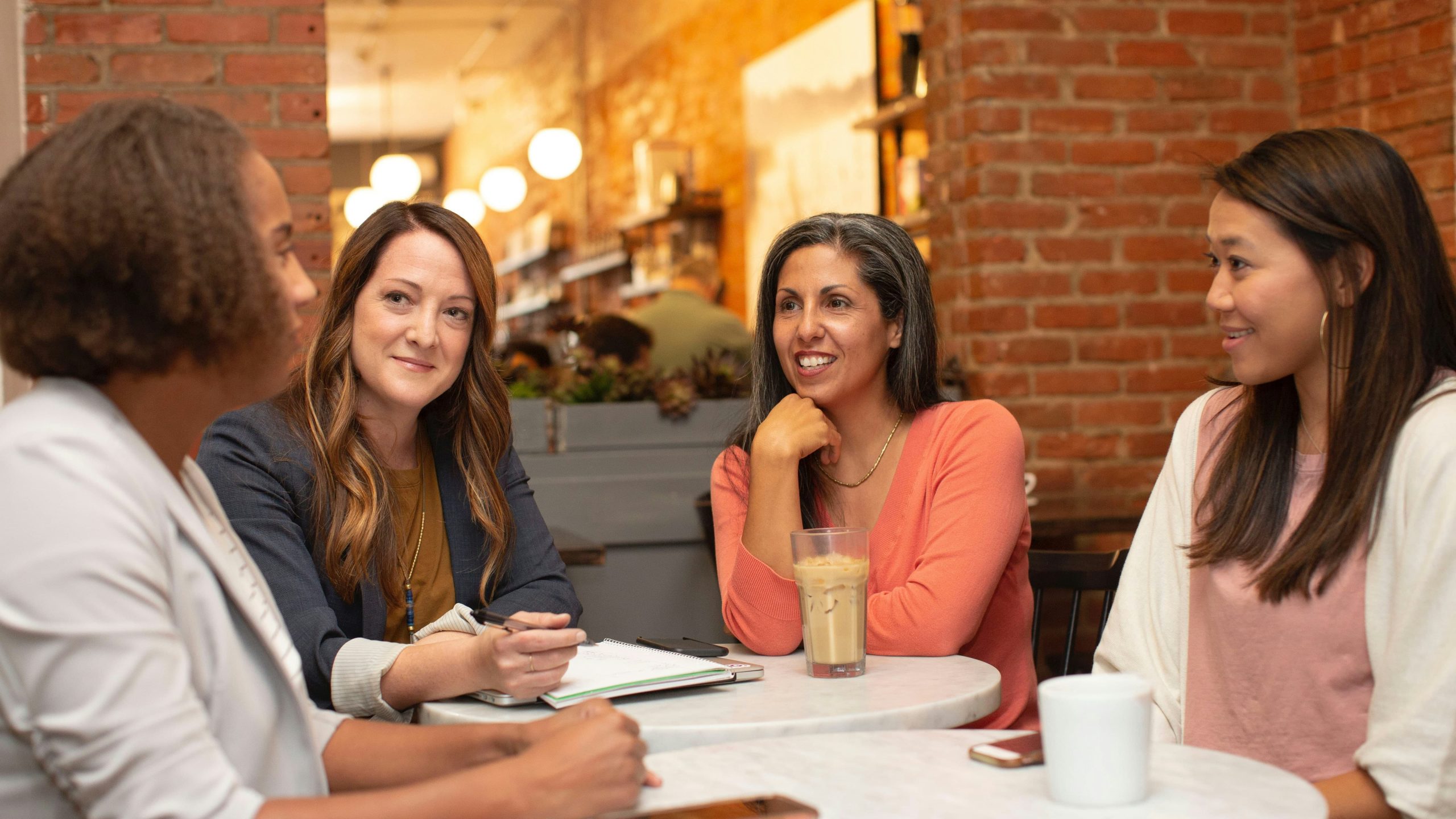 four women sat around a table in a cafe chatting