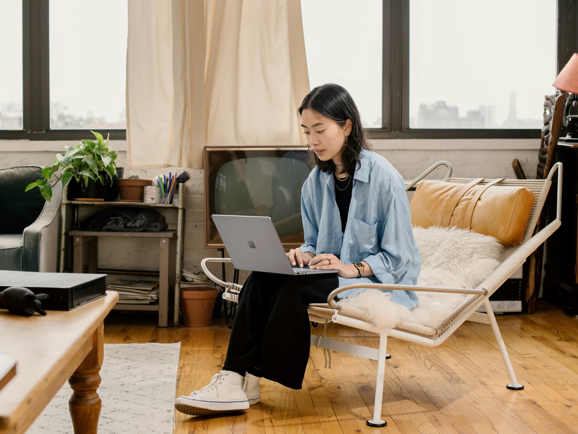 Young woman sat at in her living room with a laptop open on her knees