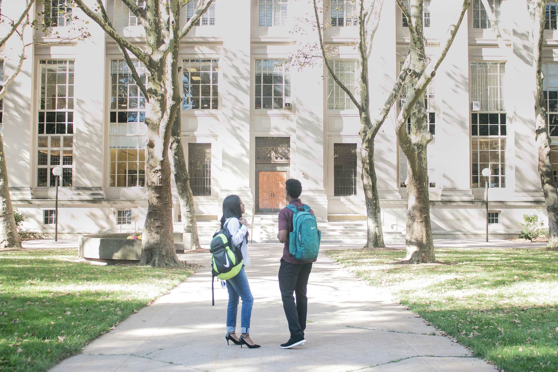 Two students with backpacks stood talking on a path on a university campus