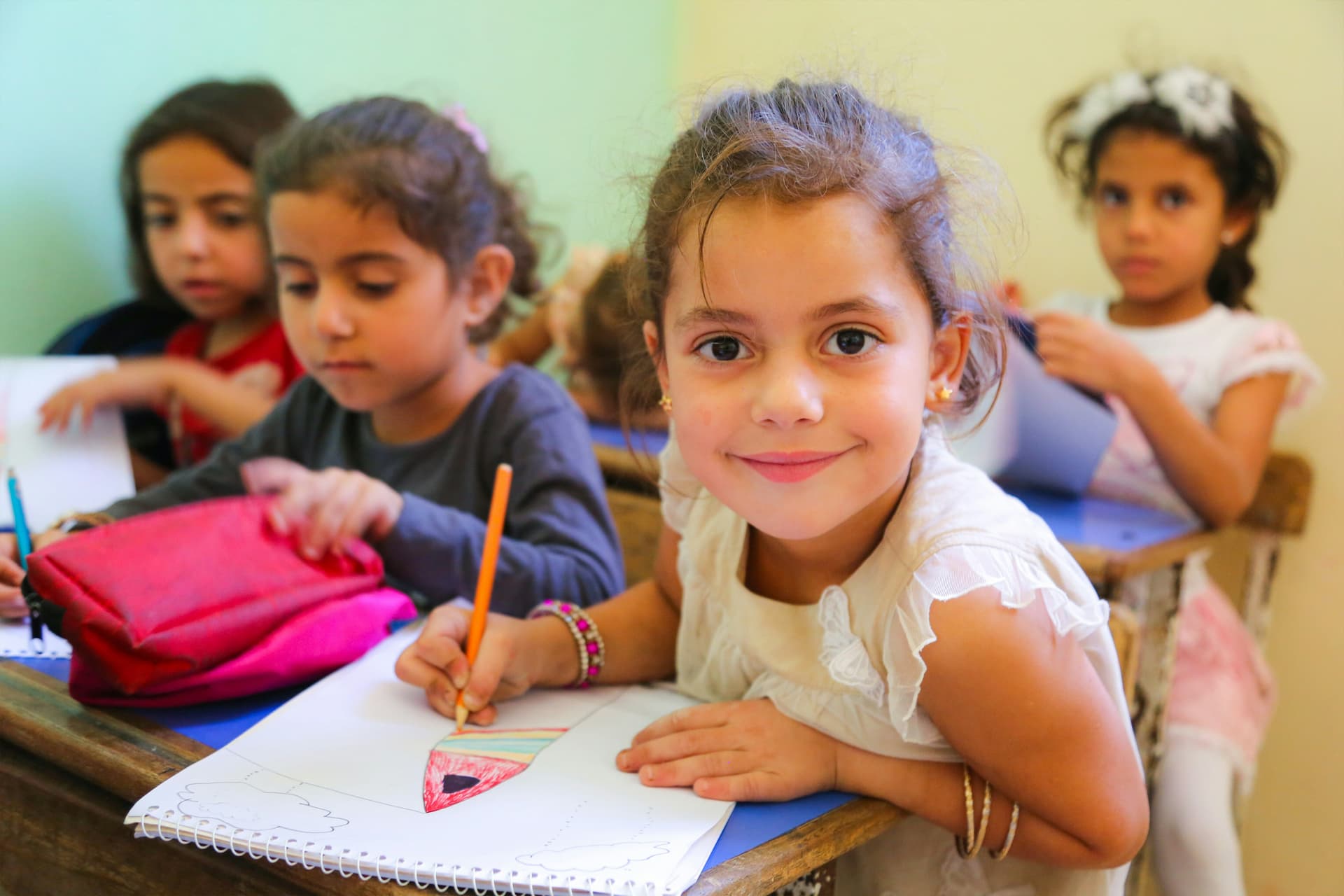 School children sat at a table colouring with one girl smiling at the camera