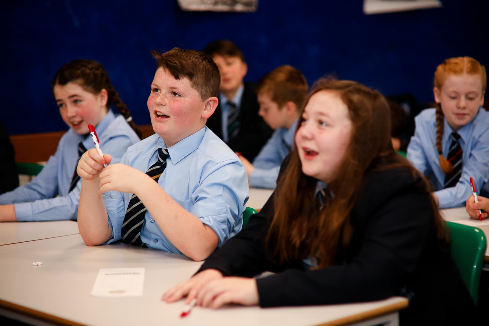 Two school pupils wearing school uniform sat at a desk smiling