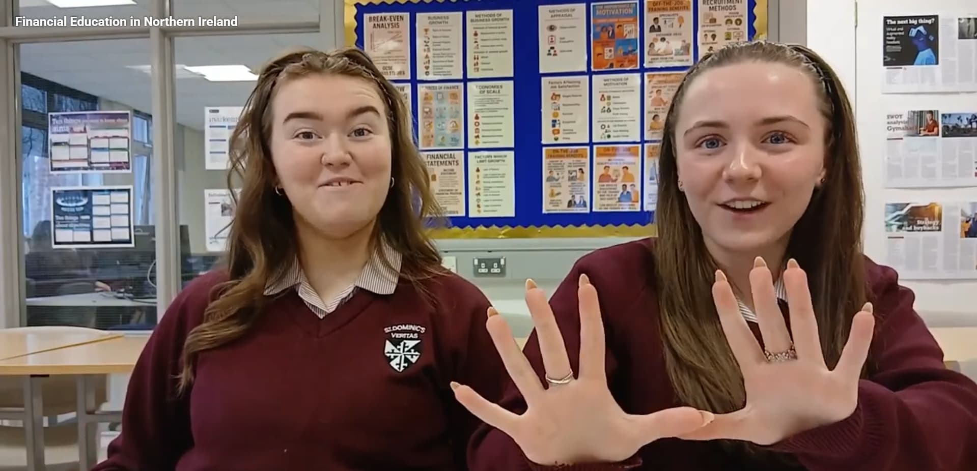 Two sixth form pupils in a classroom smiling at the camera, one of them is holding her hands to the camera showing 