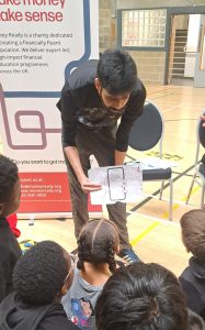 Volunteer at Money Ready showing a worksheet of a mobile phone scam to young children sat on the floor