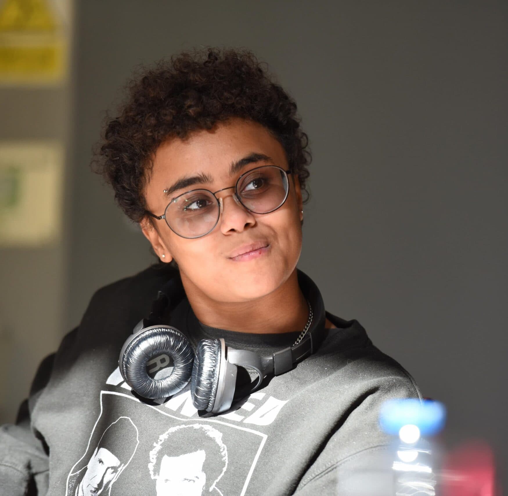 Young person wearing glasses and headphones round their neck sat smiling