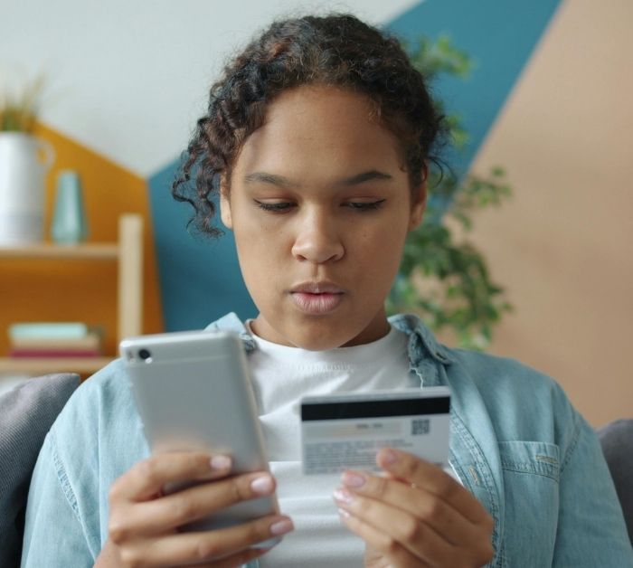 Young person using a bank card and mobile phone.