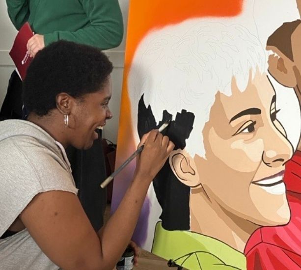 Young person smiles and paints a portrait on a large canvas.